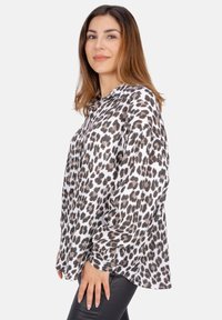Leopardenmuster-Bluse aus leichtem Stoff, mit Kragen, langen Ärmeln und lockerer Passform. Akzentuiert mit dunkelbraunen Flecken auf weißem Grund.