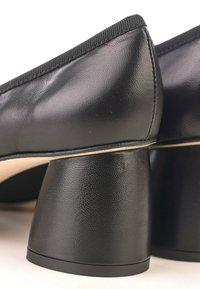 Zapatos de cuero negro con punta redonda, superficie texturizada y un tacón grueso distintivo. Bordes rematados con una suave tela acanalada.