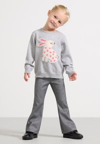 Camisola cinzenta com um desenho de coelho branco e fofo, com corações cor-de-rosa; combinada com calças cinzentas cintilantes e flare e sapatos pretos.