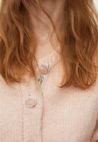 Jasnoróżowy dziergany kardigan z okrągłymi guziczkami z tkaniny, zdobiony kwiatowym haftem na dekolcie oraz teksturowaną przędzą.