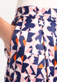 Jupe multicolore en tissu satiné, ornée d'un motif géométrique navy, rose, blanc et orange. Comprend des poches latérales.