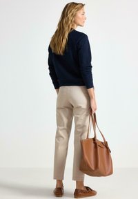 Námořnická mikina, béžové kalhoty, hnědá taška a hnědé boty. Hladká látka, uvolněný střih a vlasy po ramena.