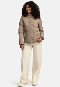Doudoune beige avec un col haut, des coutures verticales et une fermeture éclair, associée à un pantalon large crème et des baskets claires.