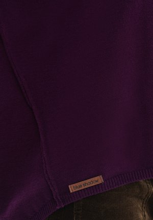 Paarse gebreide trui met een ribbelzoom en een houten label met de "blue shadow" branding. De textuur lijkt zacht met een fijne weving.