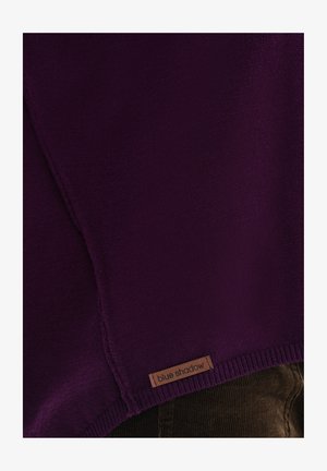 Fioletowy sweter dzianinowy z prążkowanym dołem i drewnianą metką z logo "blue shadow". Tekstura wydaje się miękka z drobnym splotem.