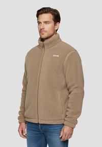 Giacca in pile beige con collo alto, chiusura a zip e tessuto strutturato. Presenta un piccolo logo sul petto e orlo e polsini elastici.