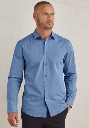Light blue button-up shirt with long sleeves, made of smooth fabric. Features a standard collar and subtle stitching details, paired with dark trousers.