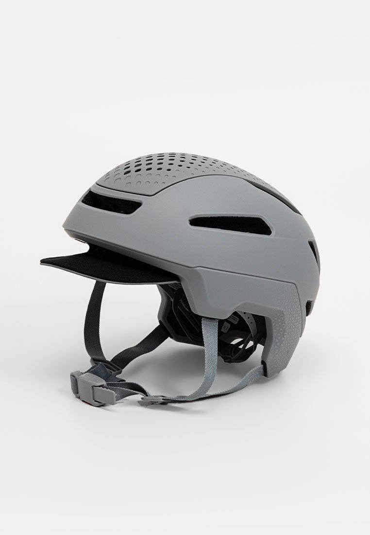 Grå cykelhjälm med en strömlinjeformad design, ventilationshål och justerbara remmar för en säker passform. Inkluderar en kort skärm.
