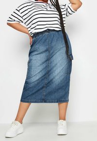 Falda midi de mezclilla con cintura elástica, que cuenta con dos bolsillos laterales y un color azul desgastado. Combinada con una camiseta de gran tamaño a rayas en blanco y negro.