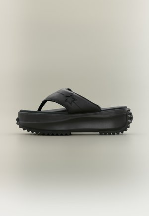 Czarna platforma sandała z grubą, teksturowaną podeszwą oraz emblematem gwiazdy na szerokim pasku przechodzącym przez górę.