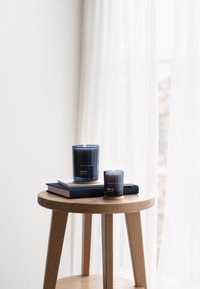 Två mörkblå glasljus, ett tänd, på en trälåda med två marinblå böcker. Ljusens etiketter läser "HAV" och inkluderar ett mönsterdesign.