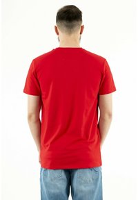 Red cotton t-shirt with a crew neckline, short sleeves, and a smooth texture, worn with light blue denim jeans.