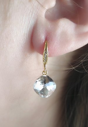 Gouden druppeloorbellen met een heldere, facetgeslepen diamantenvormige steen en een delicate ketting met kleine accentstenen.