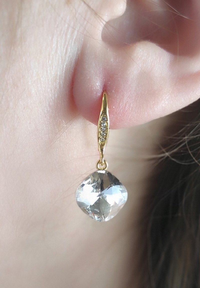 Orecchini pendenti in tonalità oro presentano una pietra chiara a forma di diamante con taglio sfaccettato e una delicata catena con piccoli stones d'accento.