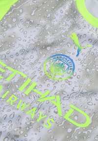 Mančesterio miesto futbolo marškinėliai su pilku vandens lašelio raštu, neoninės geltonos spalvos apykakle, Puma logotipu ir Etihad Airways rėmėjų tekstu.