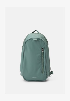 Zaino in nylon verde con una texture liscia, dotato di una tasca frontale con zip, spallacci regolabili e un piccolo logo decorativo in basso.