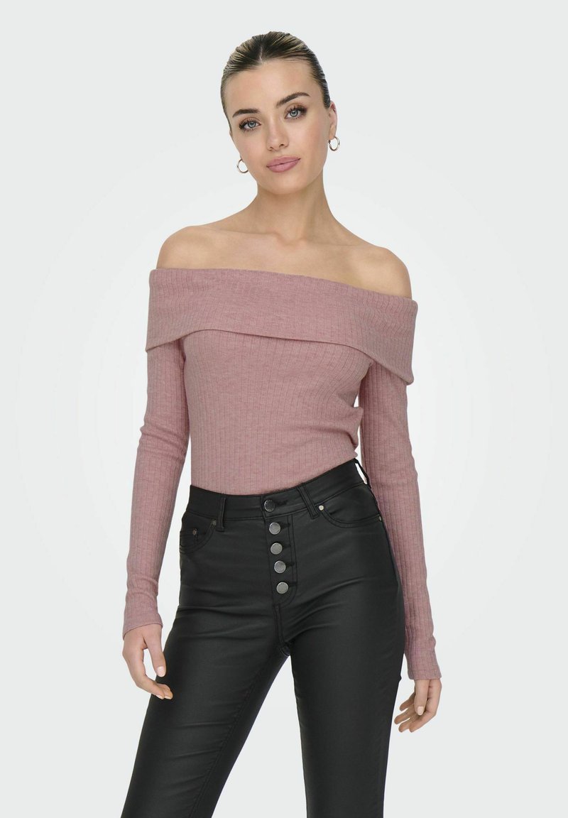 Off-the-shoulder ribbet bluse i blød lyserød, med lange ærmer og en tætsiddende pasform. Kombineret med højtaljede sorte jeans med knapdetaljer.