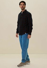 Zwarte en rode geruite shirt, met knoopsluiting, lange mouwen. Gecombineerd met lichtblauwe jeans en grijze sneakers. Eenvoudige en casual outfit.