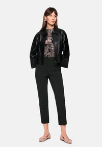 Schwarze Leder-Bomberjacke, florales Oberteil in Rosatönen, maßgeschneiderte schwarze Hose und hellrosa Ballerinas mit Schleifendetail.