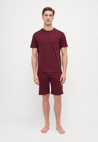Burgundy cotton t-shirt with short sleeves and pocket, paired with matching knee-length shorts, featuring a relaxed fit and soft texture.