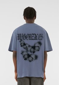 Tricou gri cu un grafic mare al unei fluturi negre și text stilizat "MYGONZA" pe spate, cu mâneci scurte și o croială lejeră.