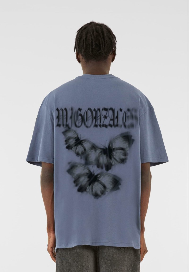 Tricou gri cu un grafic mare al unei fluturi negre și text stilizat "MYGONZA" pe spate, cu mâneci scurte și o croială lejeră.