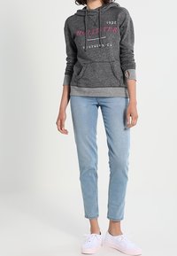 Ljust grå hoodie med rosa text, framfickor och dragsnöre. Bärs med ljusblå skinny jeans och vita sneakers. Avslappnad stil.