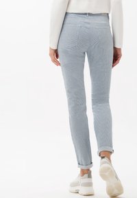 Světle modré kordové kalhoty s užším střihem, se zatočenými nohavicemi a dvěma zadními kapsami. Nosič má na nohou šedé a bílé tenisky.