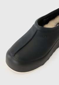 Fekete bőr slip-on cipő, lekerekített orral, vastag talppal és puha belső béléssel. Figyelemre méltó varrási részlet a felső részen.