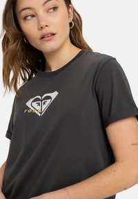 Sort kortærmet t-shirt med et kontrasterende hvidt og gyldent hjerte-logo med geometriske former. Blødt bomuldsmateriale med en afslappet pasform.