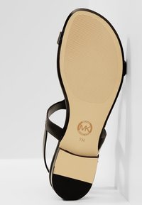 Semelle d'une sandale noire avec un dessous beige texturé, taille 7M, et logo Michael Kors près du talon.