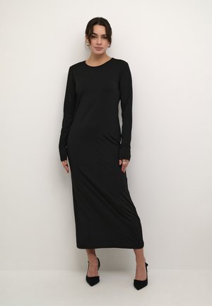 Black long-sleeve dress made of smooth fabric, featuring a straight cut and embellished with small sparkles. Paired with black pointed heels.
