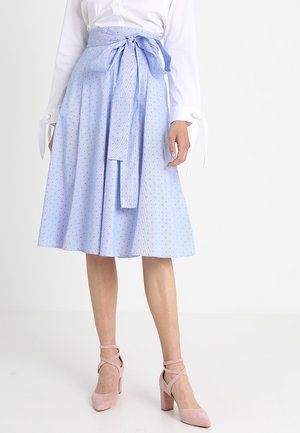 Hellblauer A-Linien-Rock mit Polka-Dot-Muster, Bund mit Schleife, kombiniert mit pinken Schuhen mit Absatz. Der Stoff wirkt glatt und leicht.