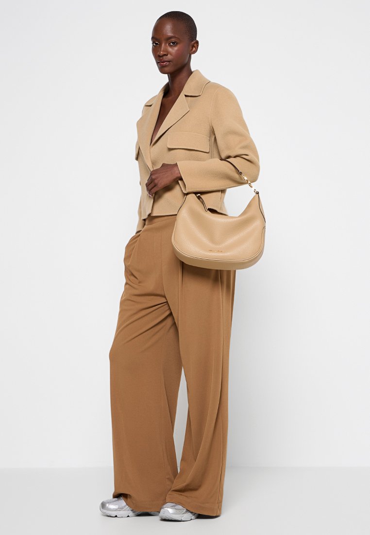 Blazer de lana beige con dos bolsillos frontales, pantalones anchos color marrón claro y un bolso de hombro marrón claro con una superficie texturizada. Zapatillas plateadas completan el look.