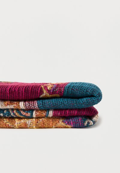 Tissu tissé plié avec des motifs multicolores, incluant des nuances de sarcelle, magenta et moutarde, présenté sur un fond blanc uni.