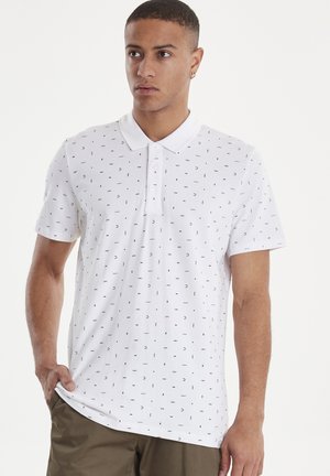 Vit polo t-shirt med ett subtilt svart geometriskt mönster, korta ärmar, en klassisk krage och knappstängning vid halsringningen.