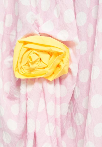 Rosa stof med store hvide prikker har en detalje af en gul stofroses. Teksturen fremstår letvægtig og let krøllet.