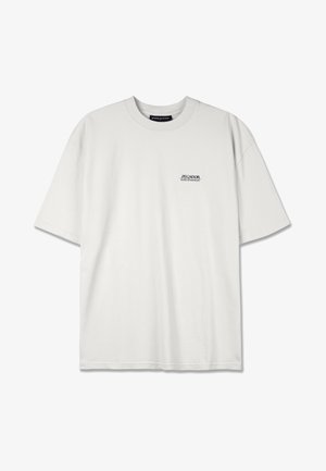 Valge puuvillane t-särk ümmarguse kaelusega, lühikeste varrukatega ja väikese musta trükitud logoga vasakul rinnal, millel on mugav lõige.