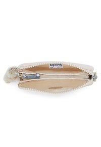 Světle béžová kabelka na zip s nadýchaným třásní, vnitřní kapsa na zip a štítek "KIPLING LIVE LIGHT". Hladká textilie.