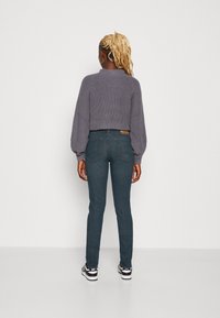 Šedý pletený svetr s nafouknutými rukávy a kulatým výstřihem, kombinovaný s tmavě modrými slim džíny a černobílými teniskami.