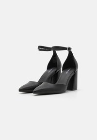 Black high-heeled shoes with a pointed toe design, smooth leather material, ankle strap with buckle, and a chunky block heel.