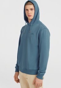 Mėlyna hoodie su raišteliais, įrengtu dangteliu, gumuotais rankogaliais ir priekinėmis logo. Pagaminta iš minkštos medžiagos su glotnia tekstūra.