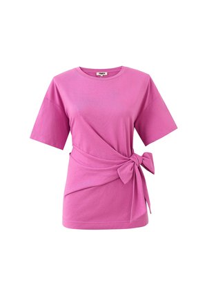 Haut rose vif à manches courtes avec un col rond et un tissu noué en nœud à la taille sur un fond blanc uni.