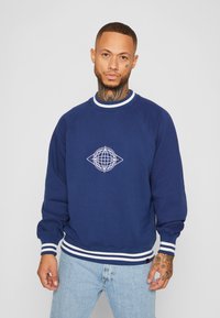 Marineblå sweatshirt med hvide stribede manschetter og kant, med et hvidt globusgrafik på brystet. Blødt stof og afslappet pasform.