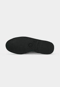 Semelle de chaussure noire avec motif d'adhérence texturé, logo de la marque et texte « NON-MARKING » visible sur fond blanc.
