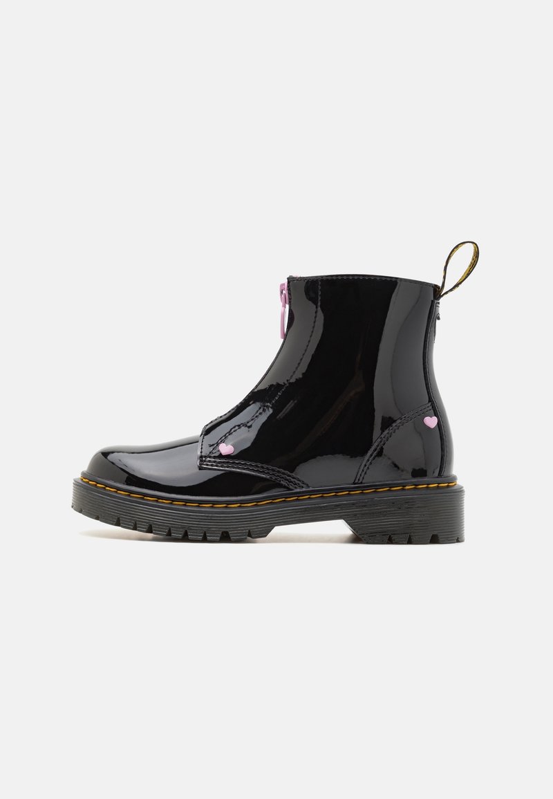 Bottine noire brillante à talon avec semelle épaisse à crampons et couture jaune, décorée de petits détails en forme de cœur rose et d'une languette arrière.