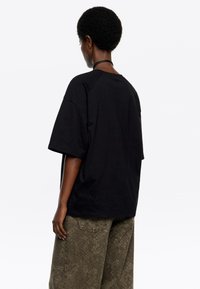 T-shirt nera oversize con girocollo e maniche corte, realizzata in morbido cotone. Abbinata a pantaloni larghi kaki con motivo.