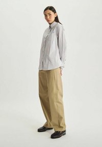 Chemise boutonnée en tissu léger avec des rayures verticales, associée à un large pantalon beige. Elle comporte une poche à rabat et un col.