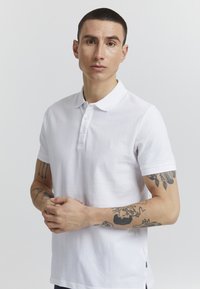 Hvit polo skjorte laget av bomull, med tre knappelukking, korte ermer og subtilt brodert logo på brystet.