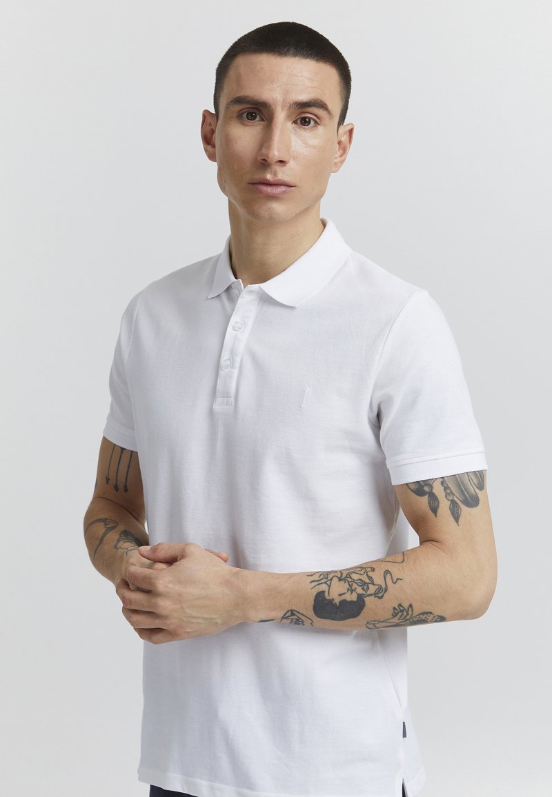 Hvit polo skjorte laget av bomull, med tre knappelukking, korte ermer og subtilt brodert logo på brystet.